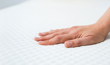 A woman placing her hand on a foam mattress