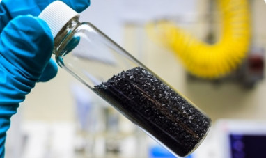 A gloved hand holding a tube of black granules