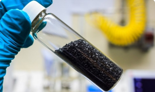 A gloved hand holding a tube of black granules