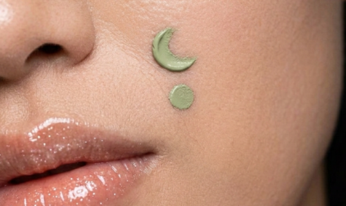 A woman with green colour corrector on her skin in the shape of a moon and a circle