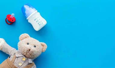 Teddy bear, dummy and baby bottle laying on a blue background